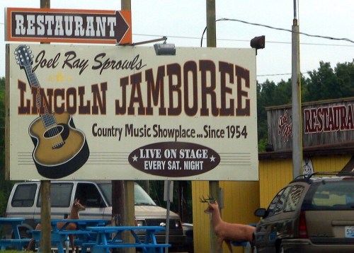 Sign for Lincoln Jamboree restaurant featuring a guitar, announcing live country music shows since 1954, with deer nearby.