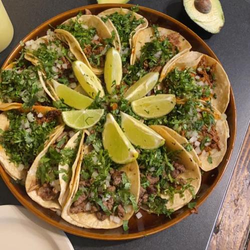 A platter of tacos topped with cilantro, onions, and lime wedges, arranged in a circular pattern.