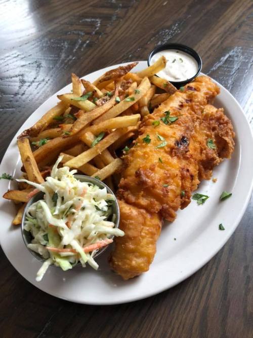 A plate of crispy fried fish fillet, golden fries, and coleslaw, served with a side of dipping sauce.