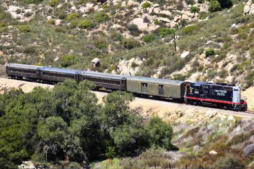 A Southern Pacific train with several cars travels through a hilly, green landscape.