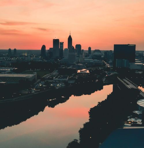 City skyline at sunset, reflecting on a river, with vibrant pink and orange hues in the sky.
