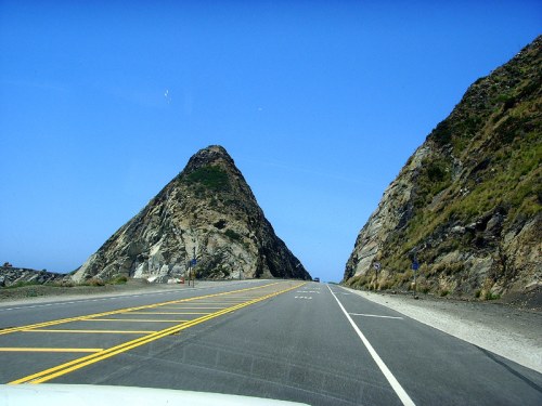 A scenic highway flanked by steep, rocky hills under a clear blue sky.