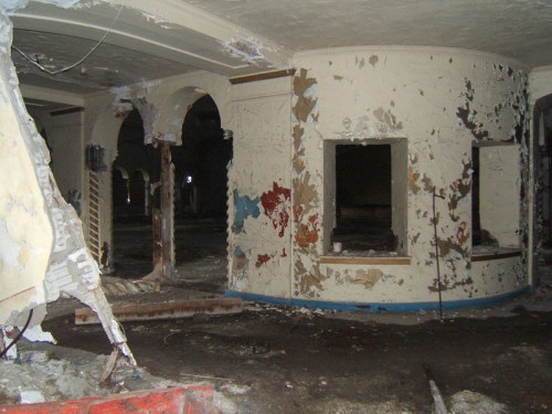 Interior of a dilapidated room with peeling paint, broken walls, and debris scattered on the floor.