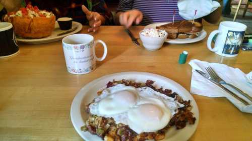 A table set with breakfast: a plate of eggs over hash browns, a mug, and dishes of toast and fruit in the background.