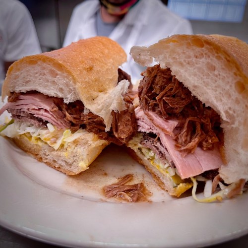 A close-up of a sandwich filled with layers of pulled pork and ham, served on a crusty bread roll.