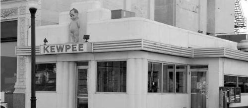 A vintage diner with the name "Kewpee" displayed prominently, featuring art deco architecture and a statue on the roof.