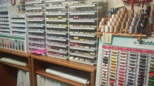 A colorful display of sewing threads organized in shelves, with spools neatly arranged on a wall.