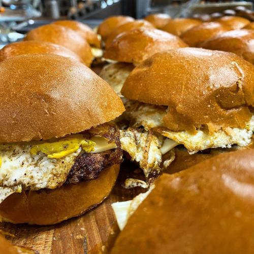 Close-up of freshly made sandwiches with fried eggs and pickles on soft, golden-brown buns.