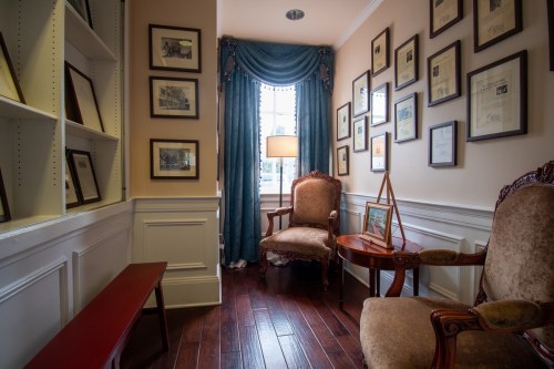 Cozy corner of a room with two armchairs, a side table, and walls adorned with framed certificates and photos.