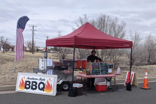 A BBQ food stand with a red canopy, serving Southern-style BBQ, featuring a menu board and an American flag nearby.