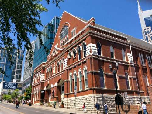 Historic brick building with arched windows, surrounded by modern skyscrapers under a clear blue sky.