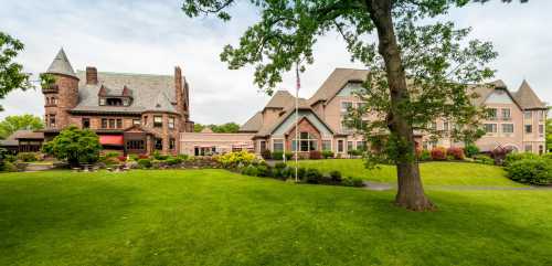 A scenic view of a large, historic mansion and a modern building surrounded by lush green lawns and trees.