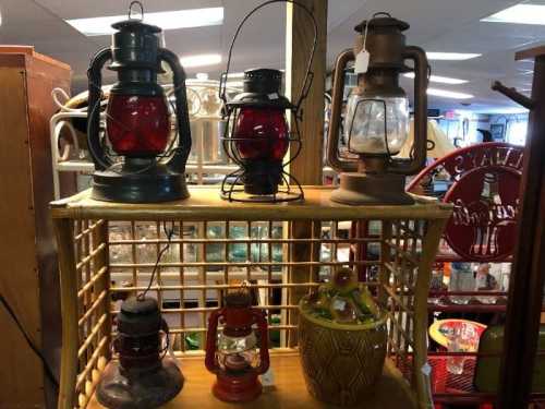 A display of vintage lanterns in various colors and styles on a wooden shelf in a shop.