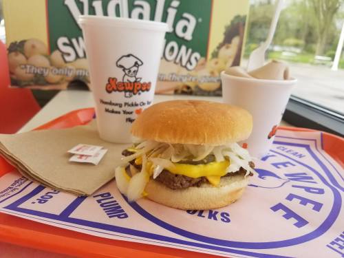 A hamburger with lettuce, onion, and cheese on a tray, accompanied by a drink and a cup of soft serve ice cream.