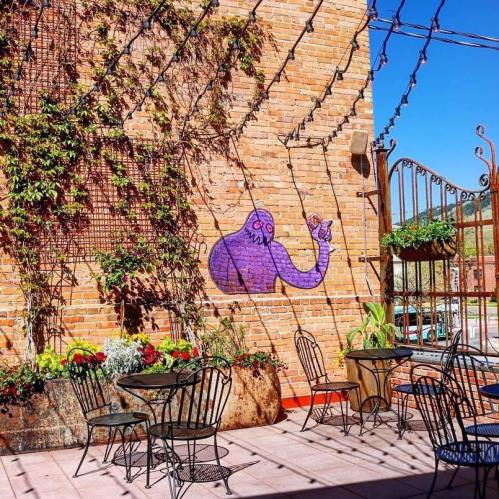 A vibrant outdoor patio with black chairs, colorful plants, and a purple mural on a brick wall.