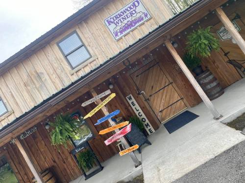 A rustic wooden building with a sign for "Kenwood Vineyards" and colorful directional signs outside.