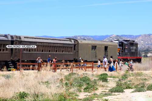 Visitors explore a railroad museum featuring vintage train cars under a clear blue sky.