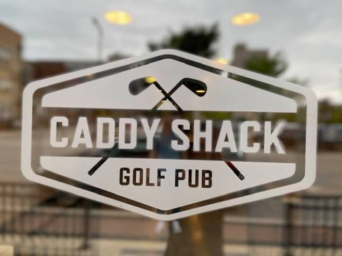 Sign for "Caddy Shack Golf Pub" featuring crossed golf clubs on a window.