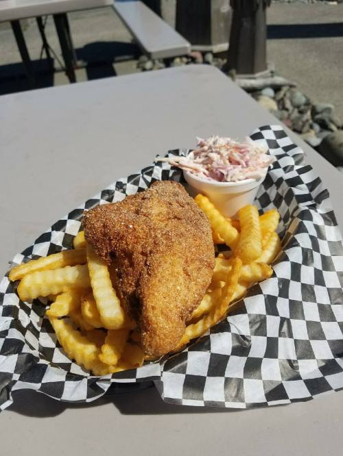 A plate of crispy fried fish served with crinkle-cut fries and a side of coleslaw in a checkered paper basket.