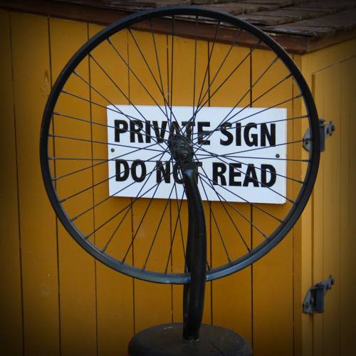 A bicycle wheel mounted on a post next to a sign that reads "Private Sign Do Not Read."