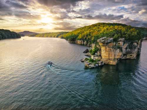 A scenic view of a river with a boat, surrounded by lush green hills and a rocky cliff under a dramatic sky.