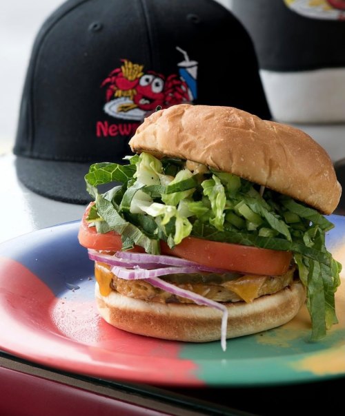 A colorful plate holds a stacked burger with lettuce, tomato, onion, and cheese, set against a blurred background.