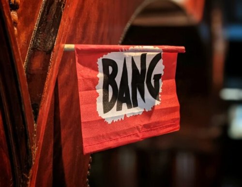 A red flag with the word "BANG" in bold black letters, hanging on a wooden surface.