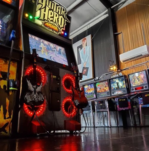 A vibrant arcade scene featuring a Guitar Hero machine and pinball games in a stylish, retro setting.