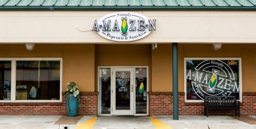Exterior of "Simply A-Maize-N Popcorn & Snacks" store with a green roof and welcoming entrance.