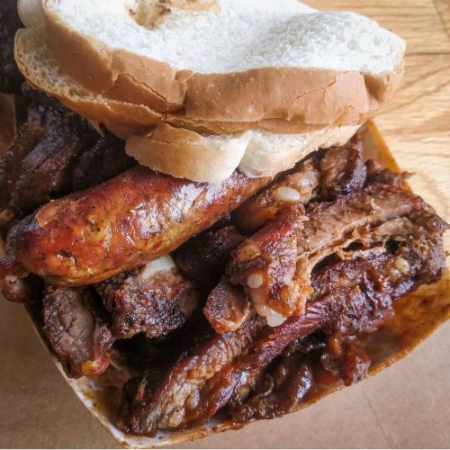 A close-up of a tray filled with various grilled meats, including ribs and sausage, topped with slices of bread.