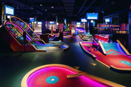 A vibrant indoor mini-golf and beer pong venue with colorful lighting and various game setups.