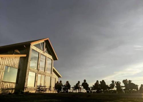 A group of people gathered outside a wooden building during sunset, with a cloudy sky in the background.