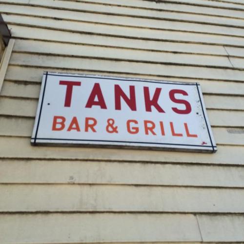 Sign for "Tanks Bar & Grill" mounted on a yellow wall.