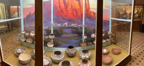 Display case featuring various traditional pottery pieces against a backdrop of a scenic landscape.