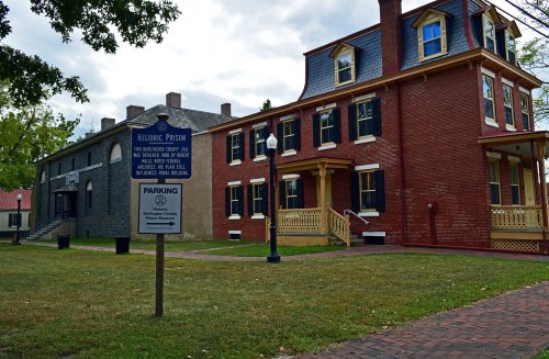 Historic prison building with a sign for parking, featuring red brick and a two-story structure with a porch.