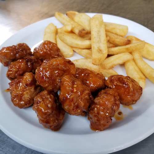 A plate of crispy chicken wings coated in a sweet sauce, served with golden French fries.