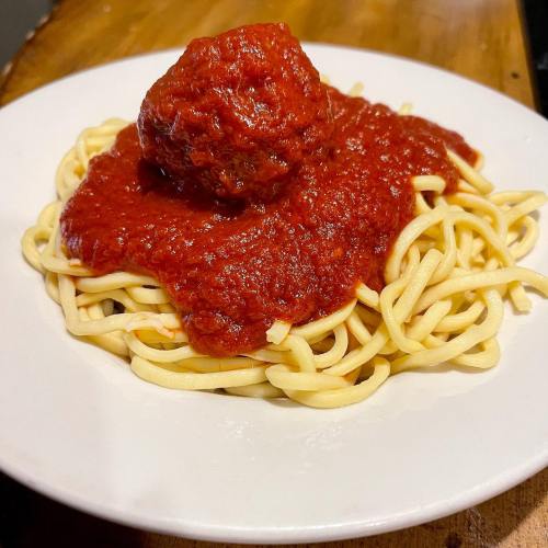A plate of spaghetti topped with marinara sauce and a large meatball.