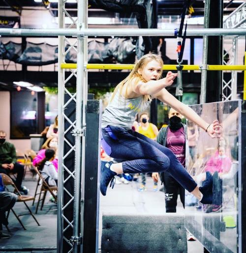 A young girl performs a dynamic move on an obstacle course, showcasing agility and focus in a gym setting.