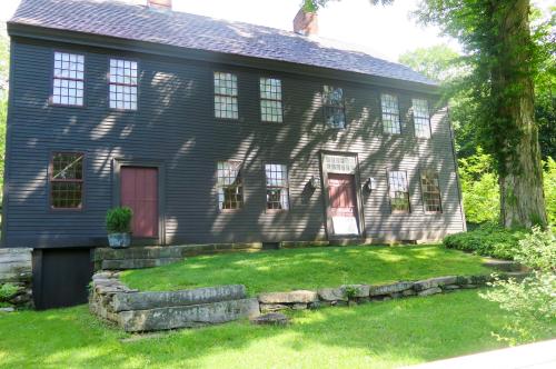 A large, dark-colored historic house with multiple windows, surrounded by green grass and trees.