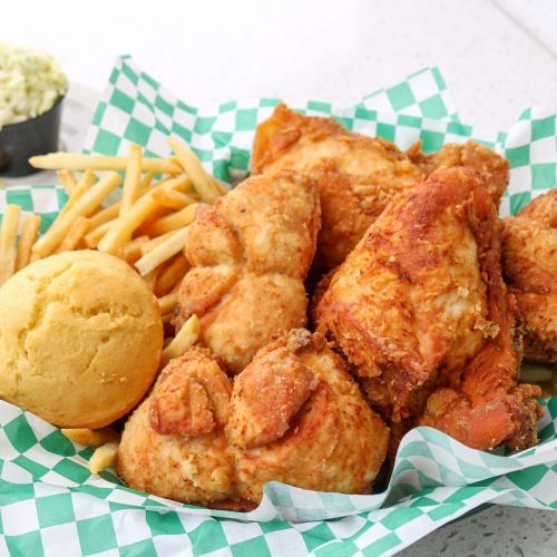 A basket of crispy fried chicken, golden cornbread, and French fries on a green checkered paper.