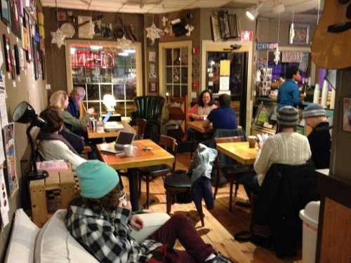 A cozy café scene with people sitting at tables, some working on laptops, and a warm, inviting atmosphere.