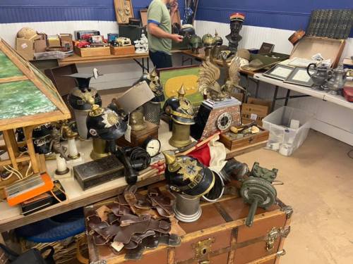 A cluttered table filled with various antique items, including busts, clocks, and decorative objects.
