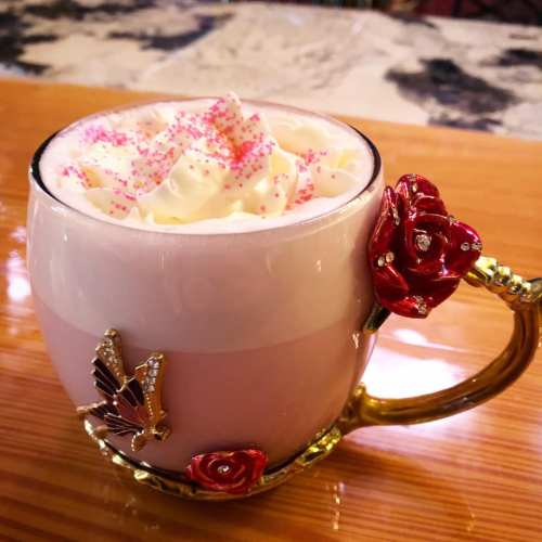 A decorative pink mug with whipped cream and pink sprinkles, adorned with rose and butterfly embellishments.