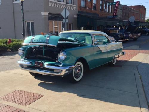 A vintage turquoise car parked on a street, showcasing its open hood and classic design.