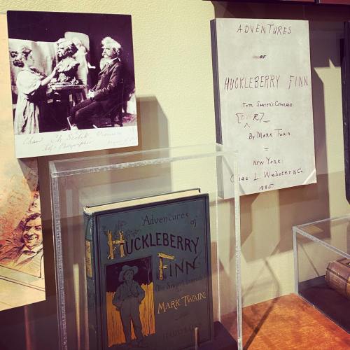 A display featuring "Adventures of Huckleberry Finn" by Mark Twain, alongside a historical photograph.