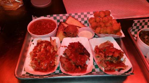 A tray of barbecue dishes featuring tacos, baked beans, cornbread, and fried okra, all served with sauce.