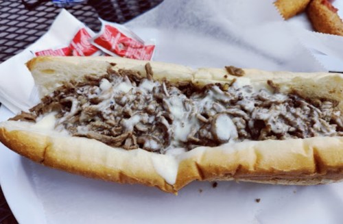 A close-up of a cheesesteak sandwich filled with shredded beef and melted cheese on a hoagie roll.