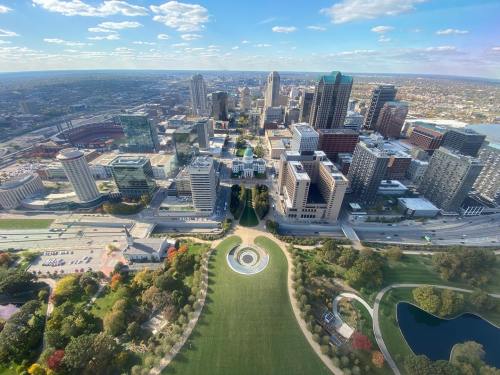 Aerial view of a city skyline with green parks, roads, and buildings under a clear blue sky.