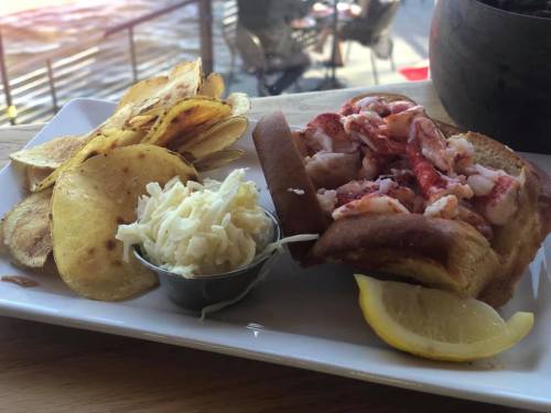 A plate featuring a lobster roll with lemon, coleslaw, and crispy potato chips.