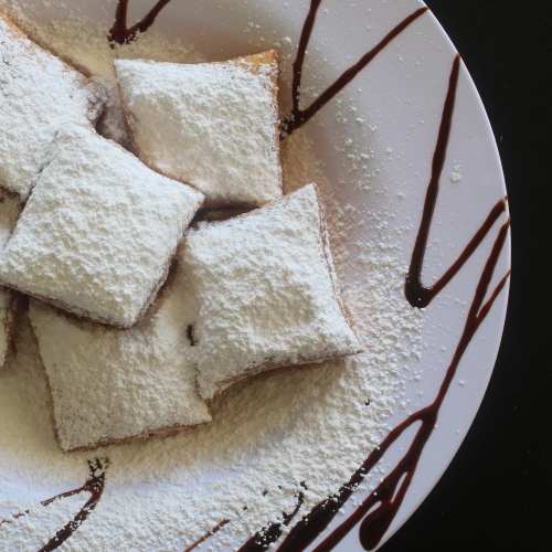 A plate of powdered sugar-dusted pastries drizzled with chocolate sauce.